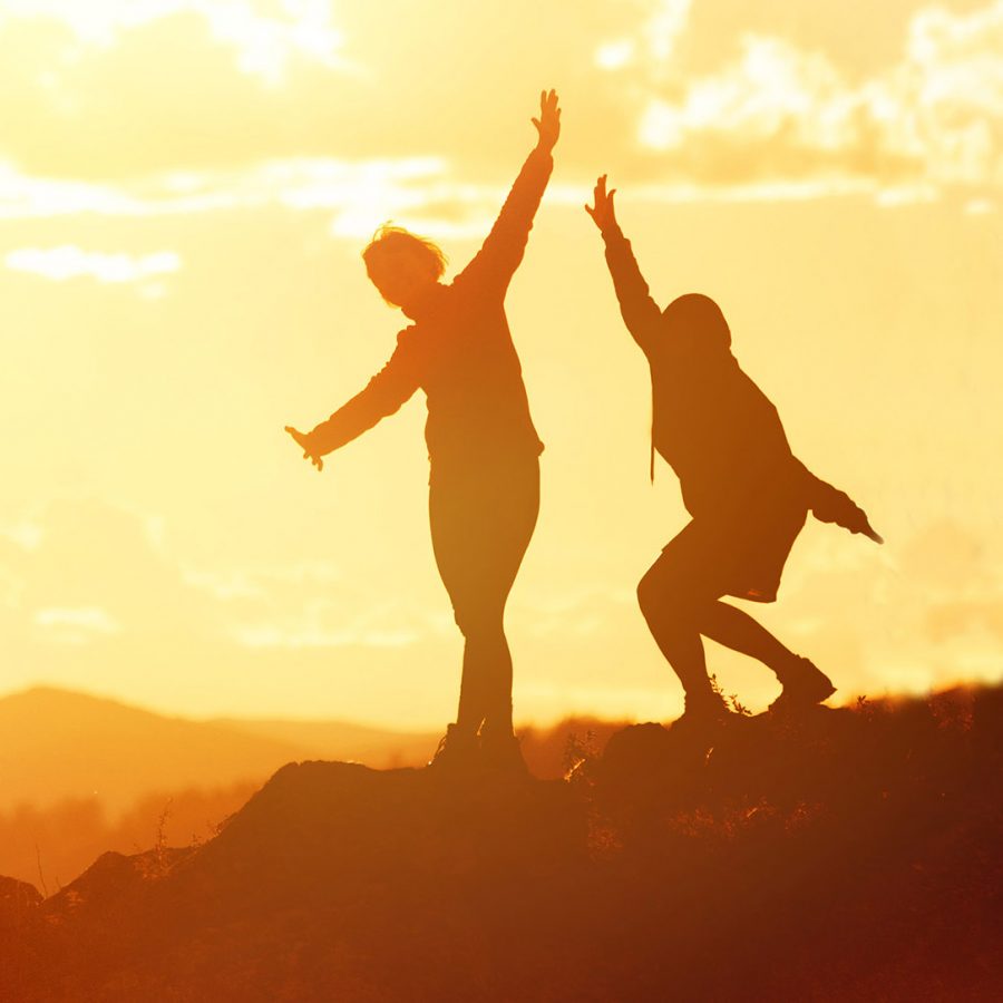 Big group of happy friends or big family silhouettes stands and having fun at sunset mountains.